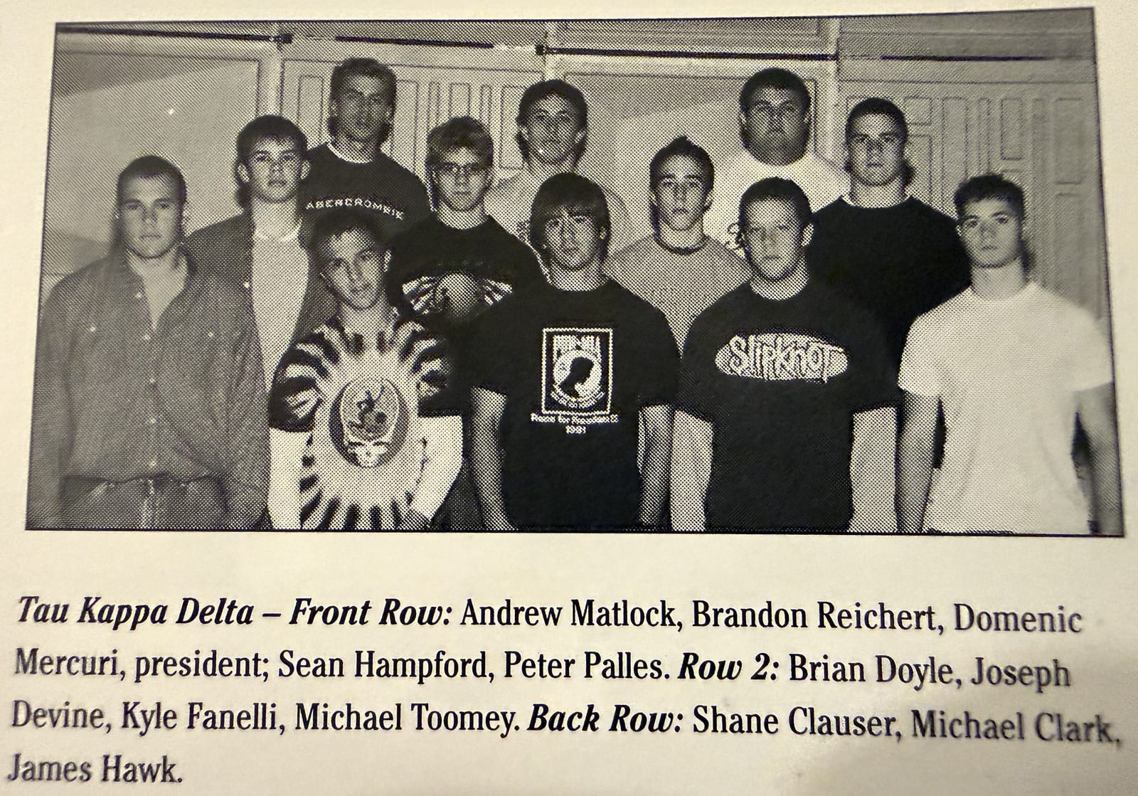 A black-and-white yearbook group photograph of about a dozen young men in two rows in front of lockers, above a printed caption listing their names.