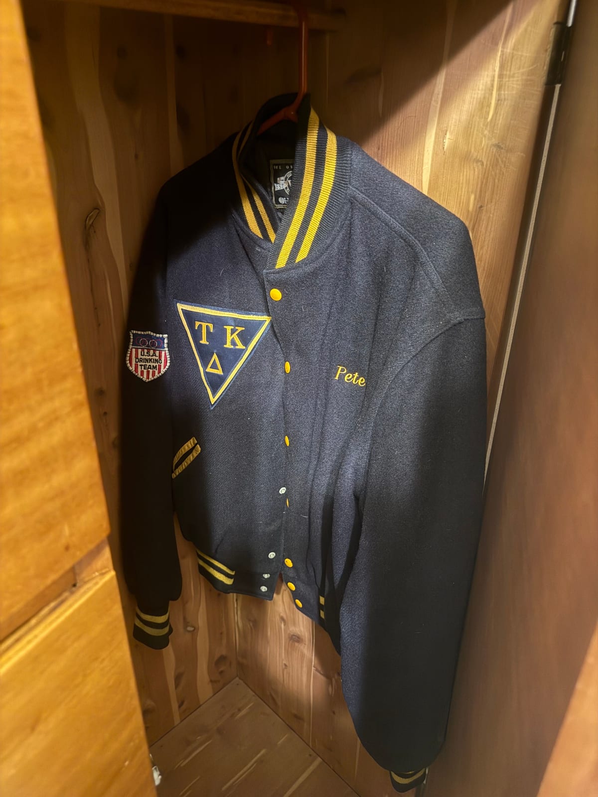 A navy wool-and-leather letter jacket with gold trim, "Pete" embroidered in gold script and a gold triangular Tau Kappa Delta emblem on the chest.